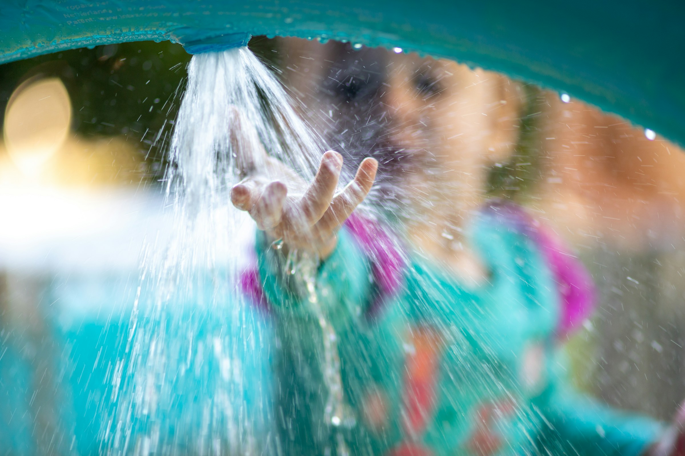 A child holds their hand under a spout spraying water.