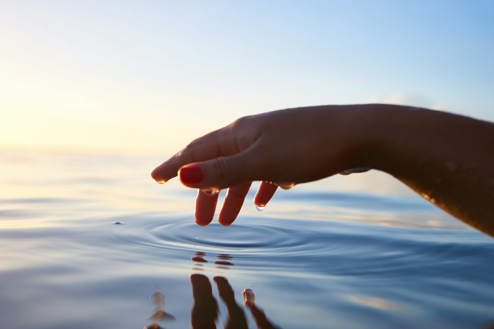 A dripping wet hand hovers over rippling water.