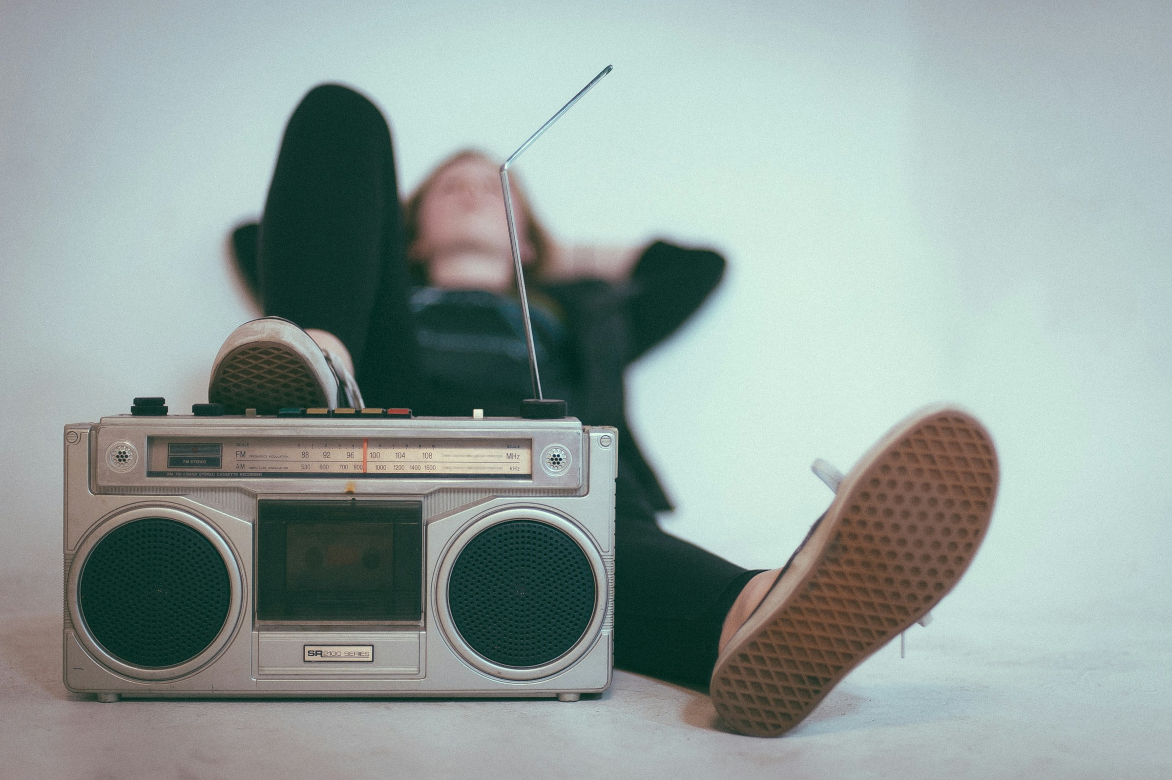 A person lays back with one foot propped up on a vintage boombox.