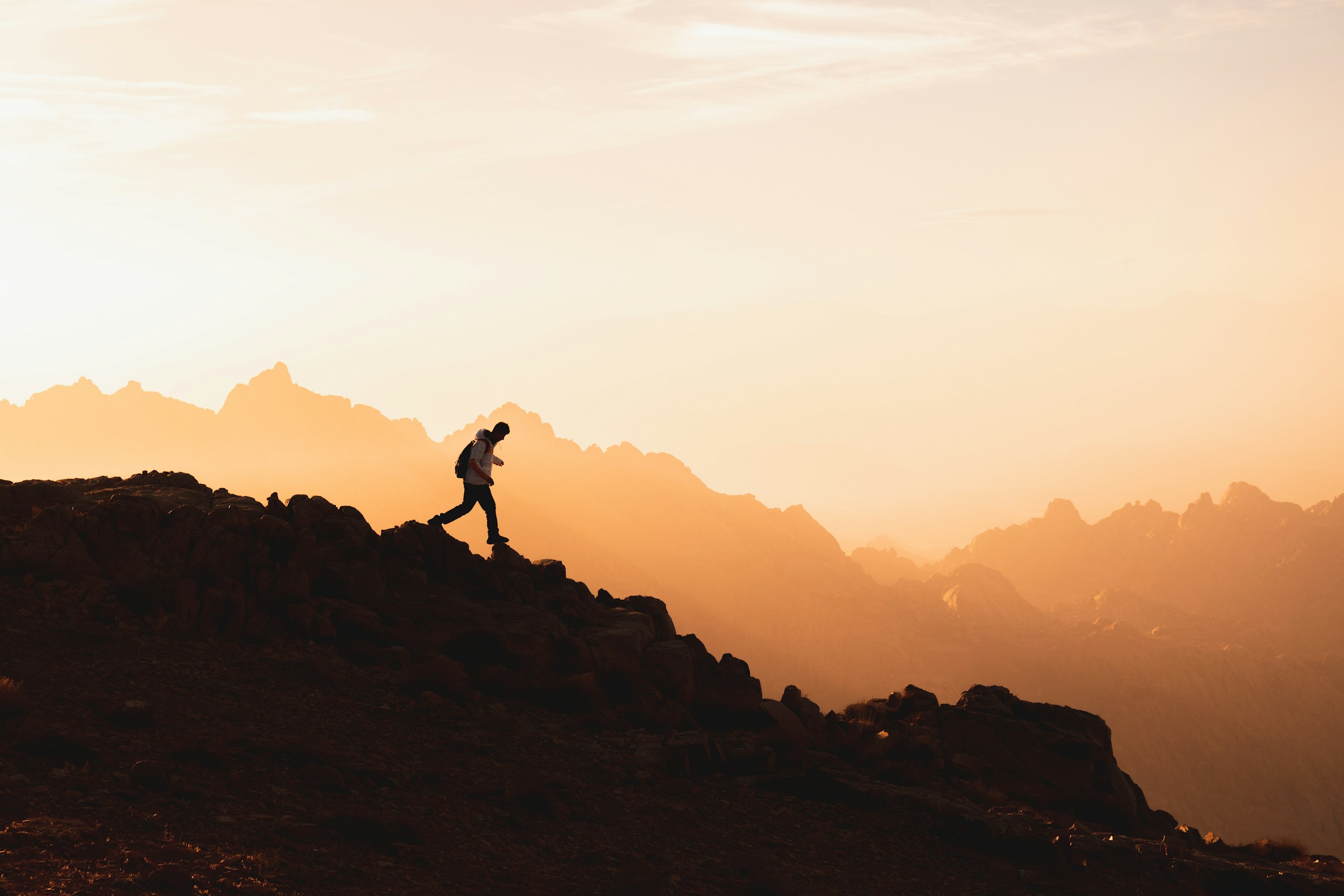A person wearing a backpack steps along a rocky ridge line.
