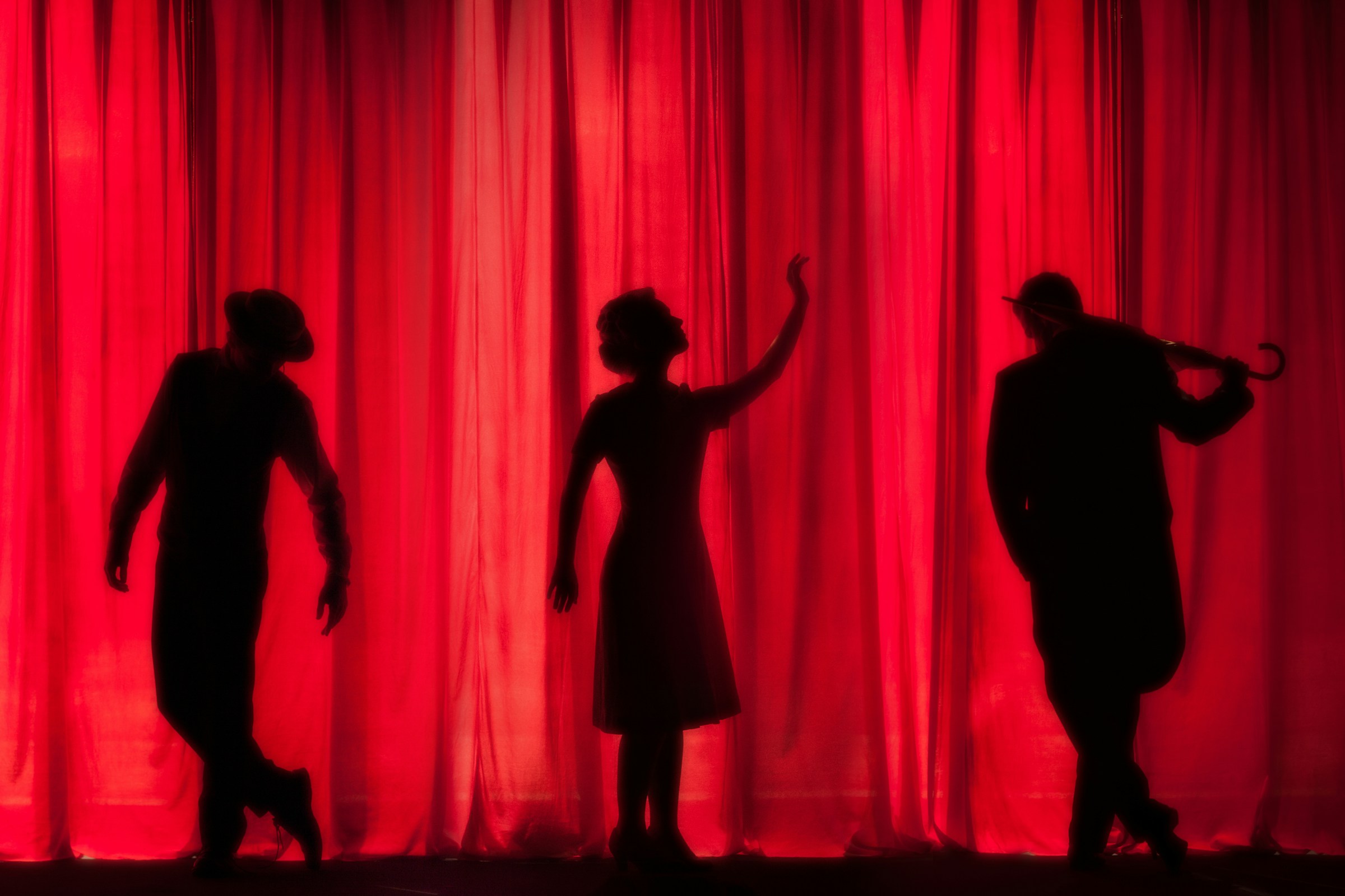 The silhouettes of three people against a red theater curtain.