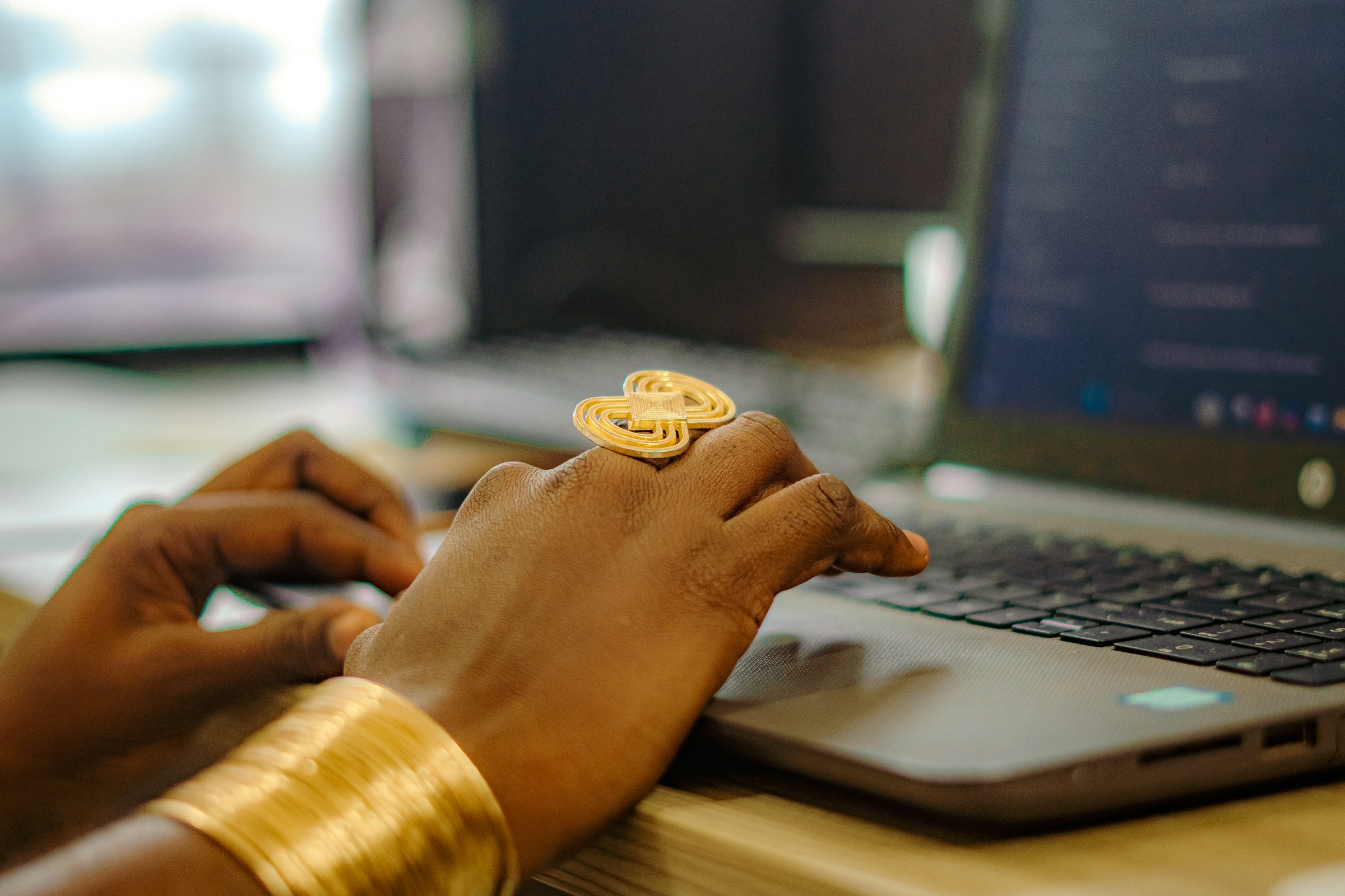 Hands wearing a big gold ring and a gold bracelet type on a laptop.
