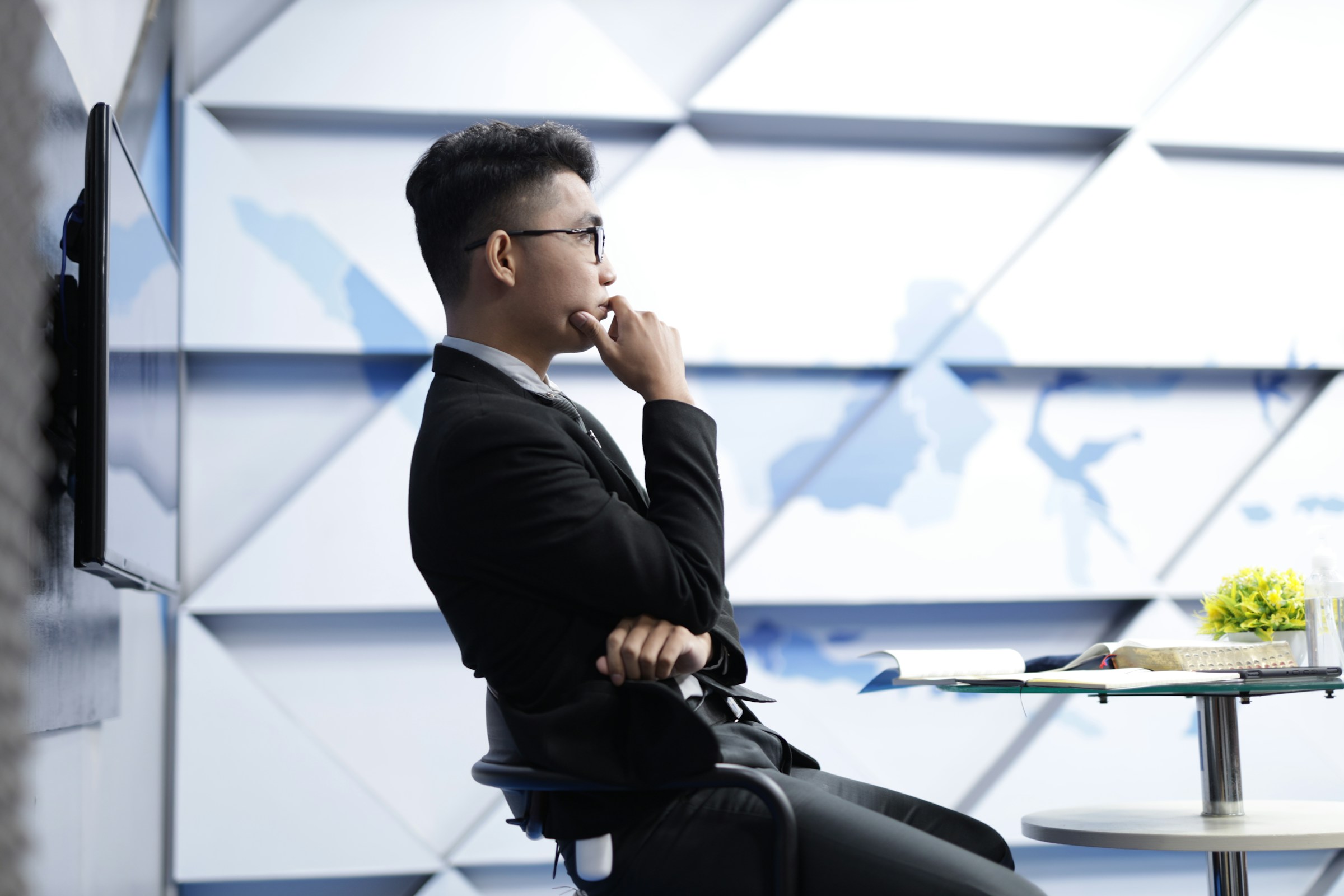A person leans back in a chair in a modern office space and holds their hand to their mouth as if thinking.