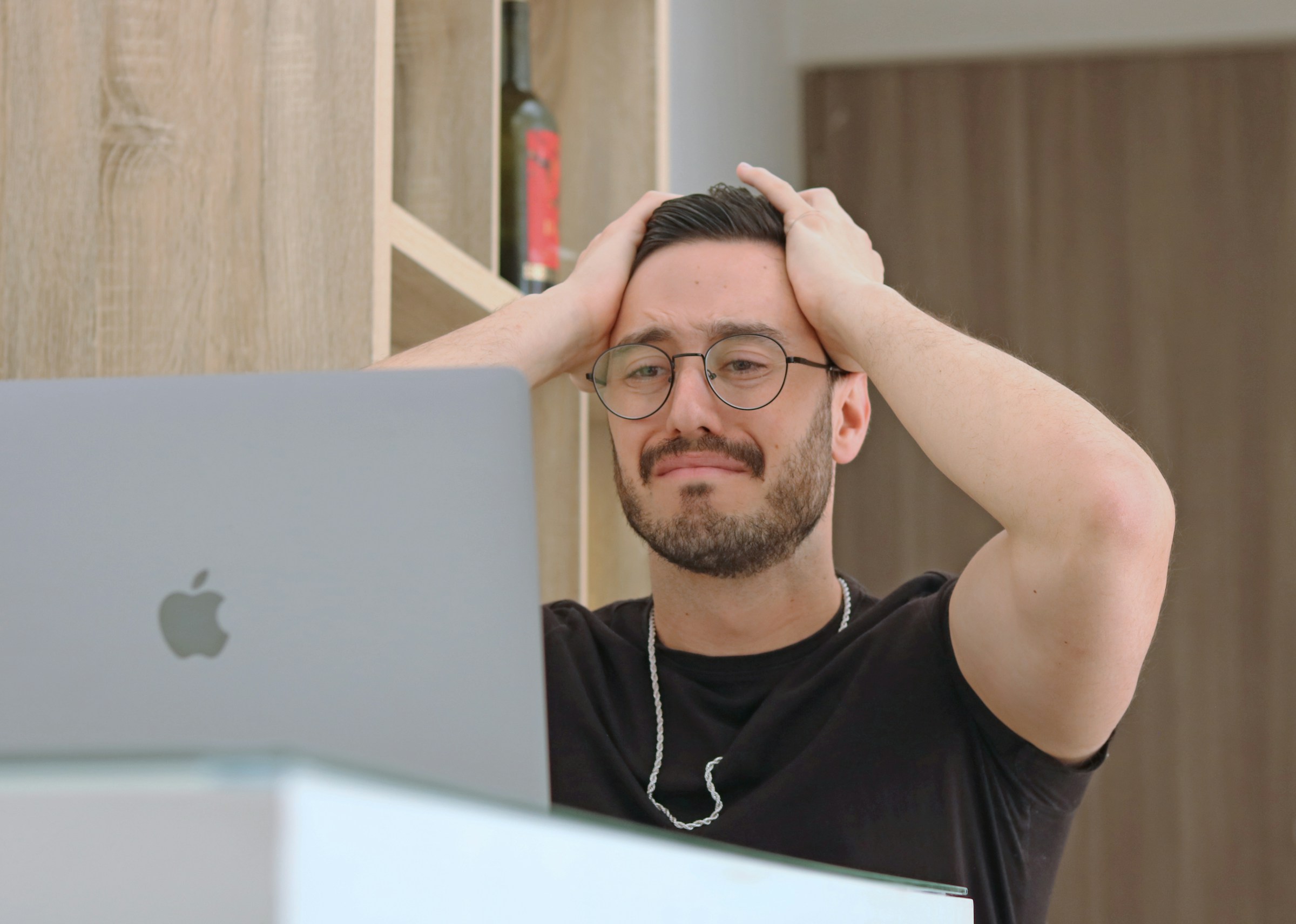 A stressed-looking person holds their head and stares at a laptop screen.