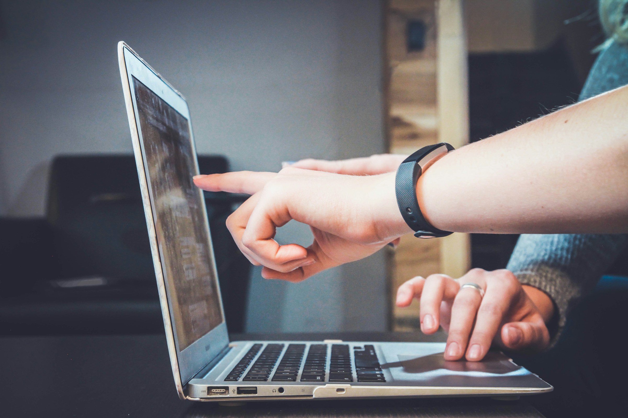Hands point at the screen of an open laptop.