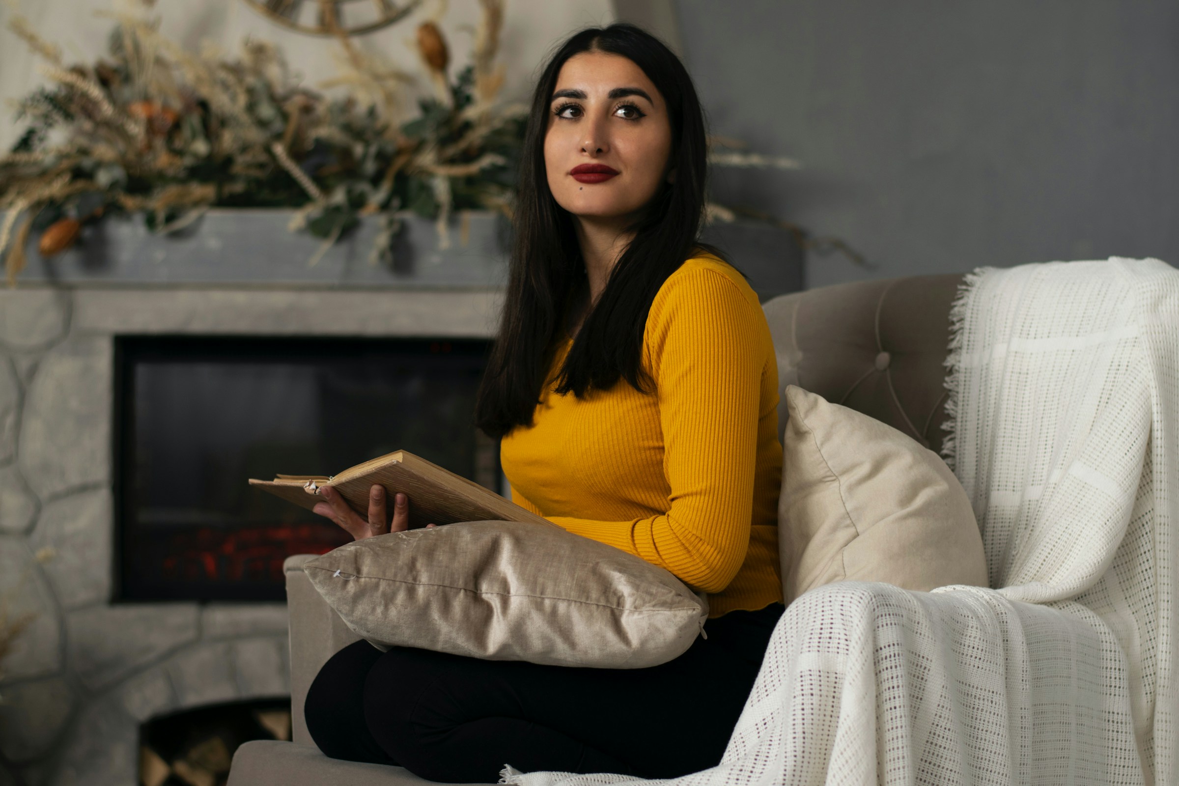 A person sits on a chair holding a book and looking off to the side.