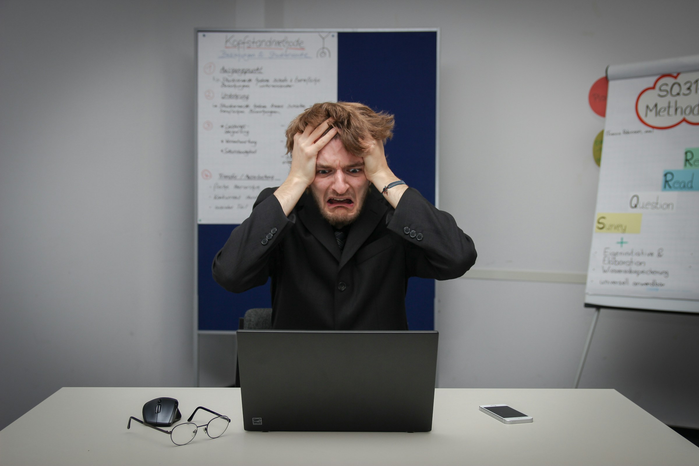 A person clutches their head and stares at a laptop screen in horror.