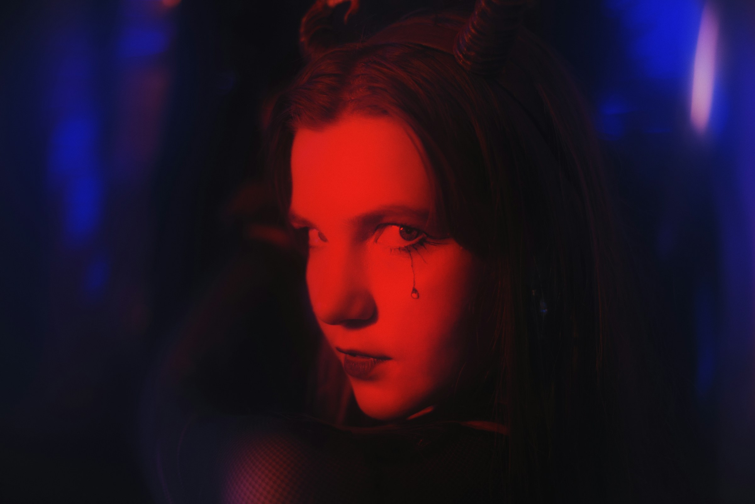 A person whose face is cast in red light stares at the viewer, unsmiling.