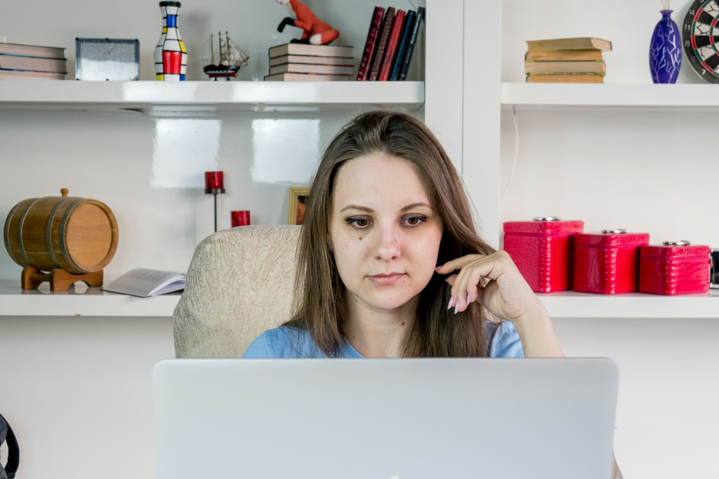 A person sits at a desk in front of a bookshelf, looking at a computer screen.