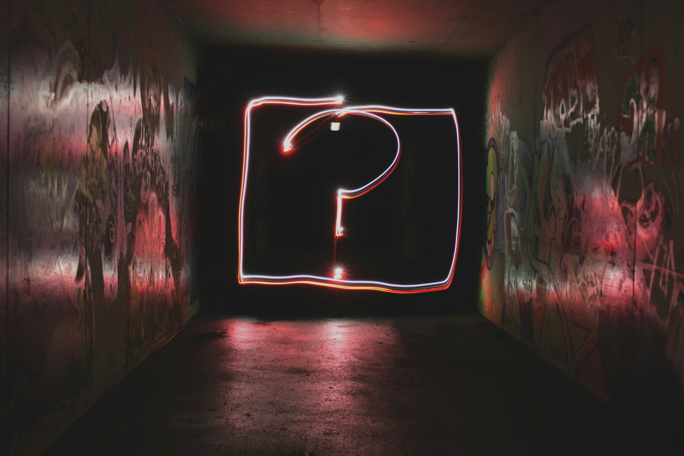 A question mark made of light at the end of a dark concrete hallway.