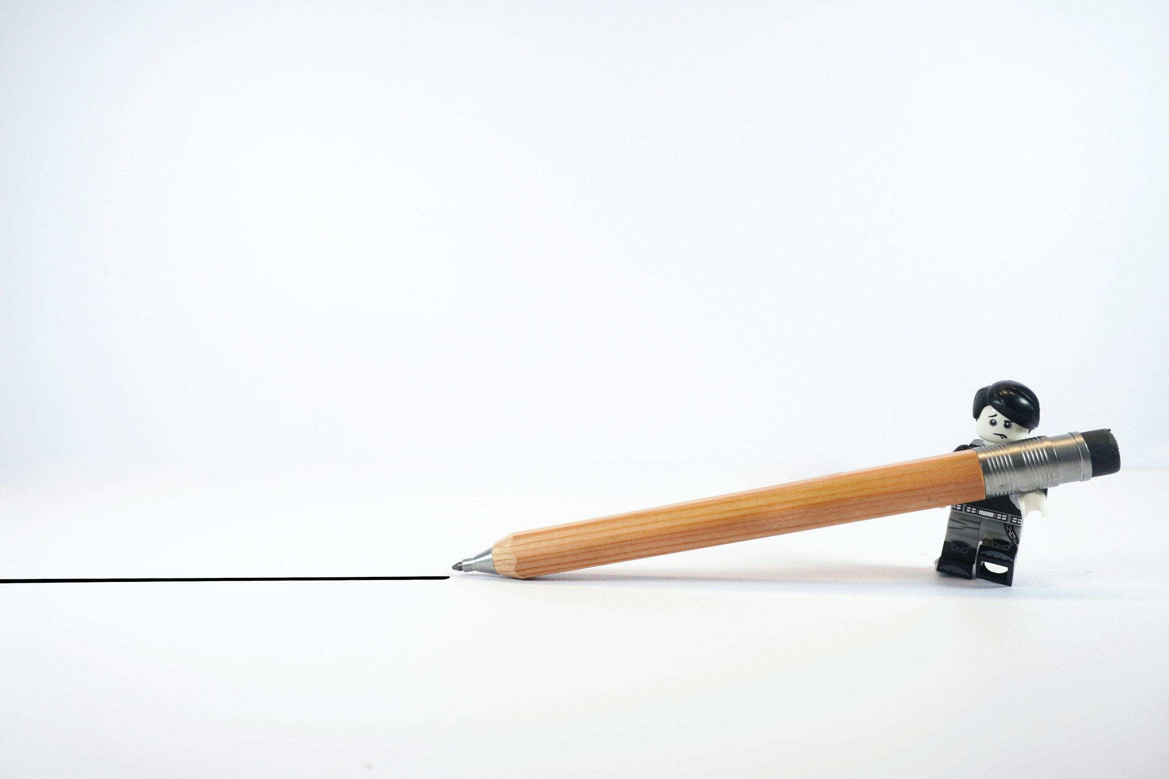 A black-and-white LEGO person appears to drag a pencil across a piece of paper, drawing a straight line.