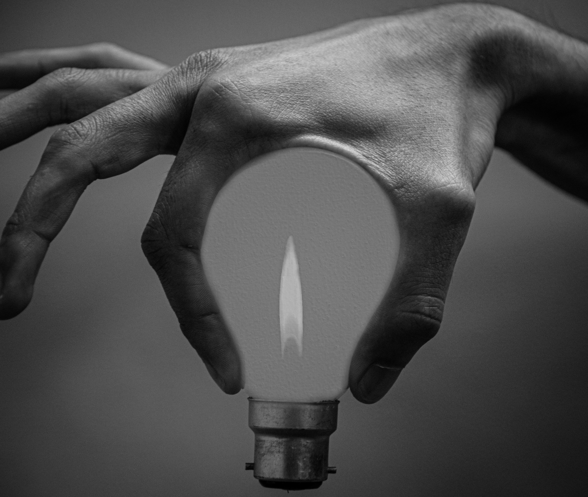 A person holds the bulb of a lightbulb between their index finger and thumb. A flame flickers inside the lightbulb.