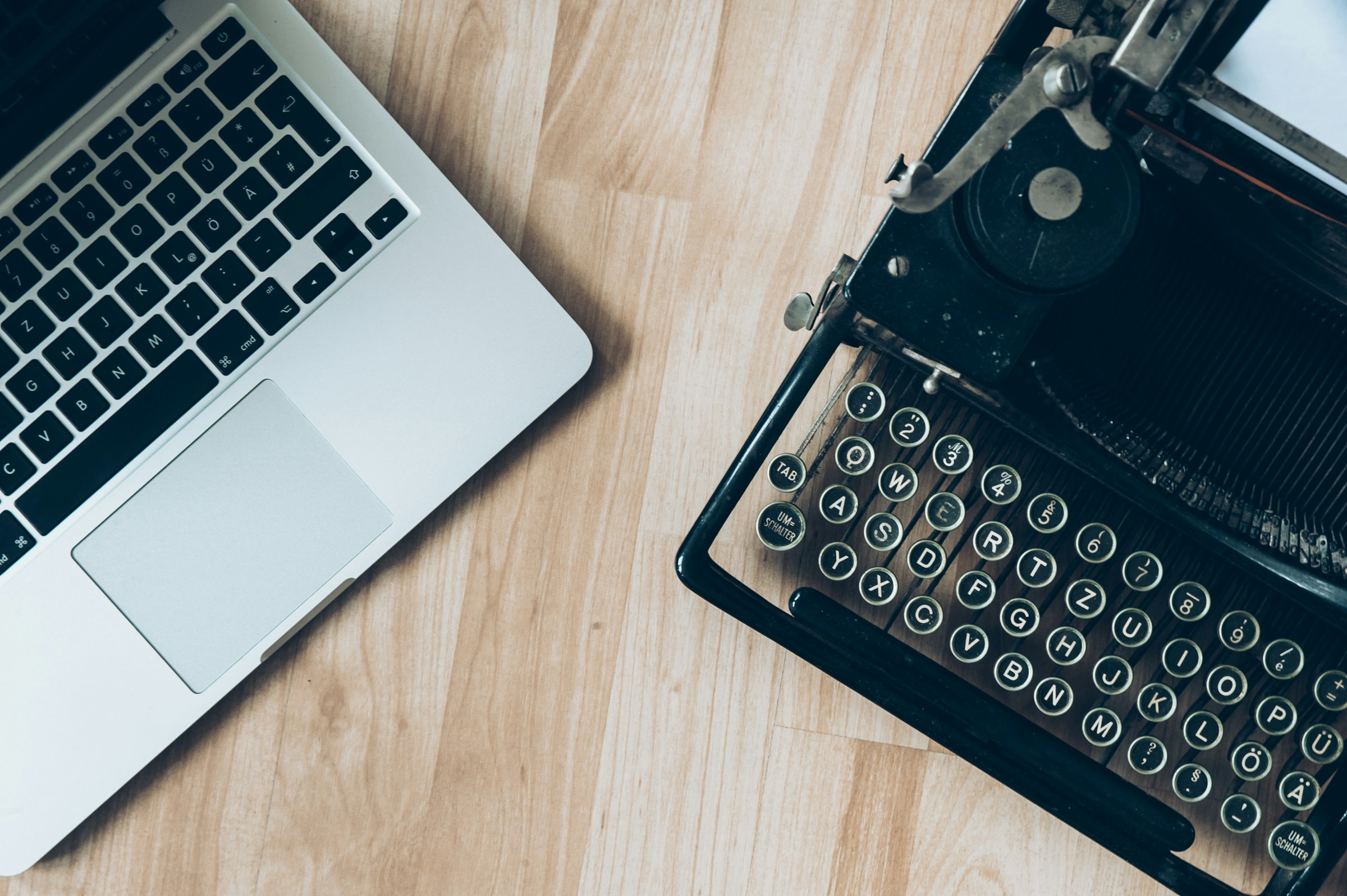 Overhead view of a laptop keyboard and a manual typewriter keyboard side by side on a wooden surface.