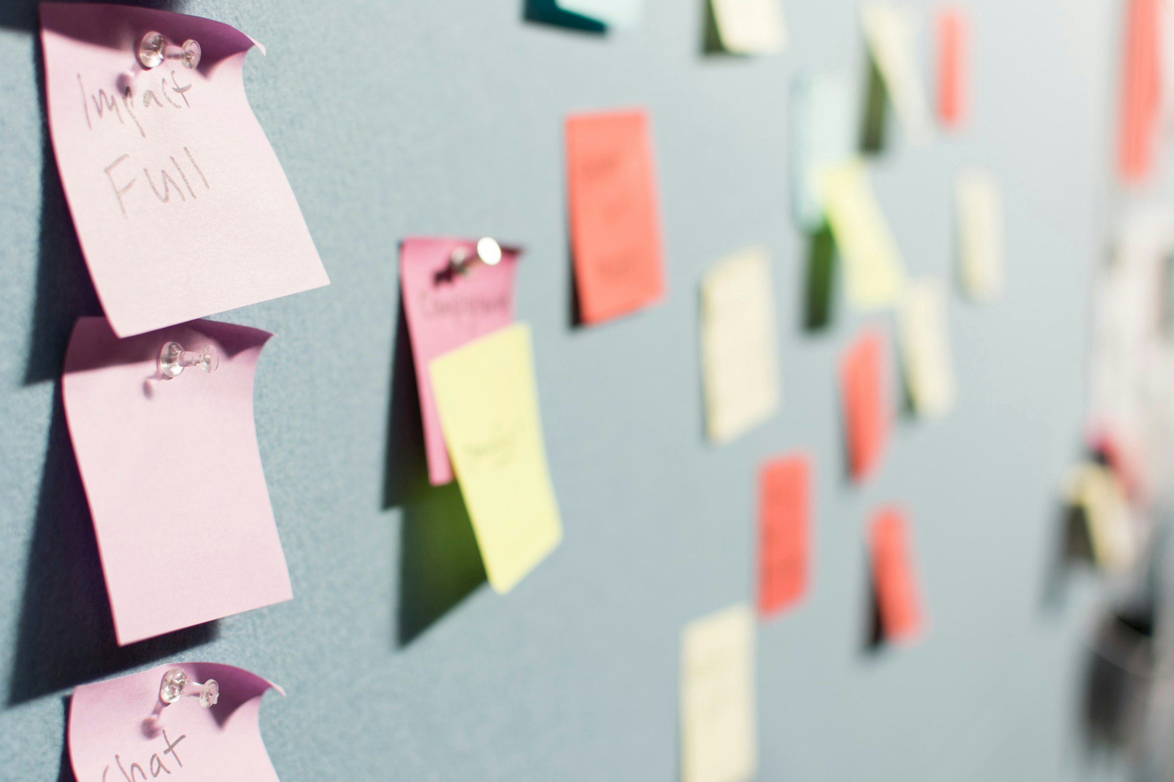 Several colorful sticky notes stuck to a dark cork board with thumb tacks.