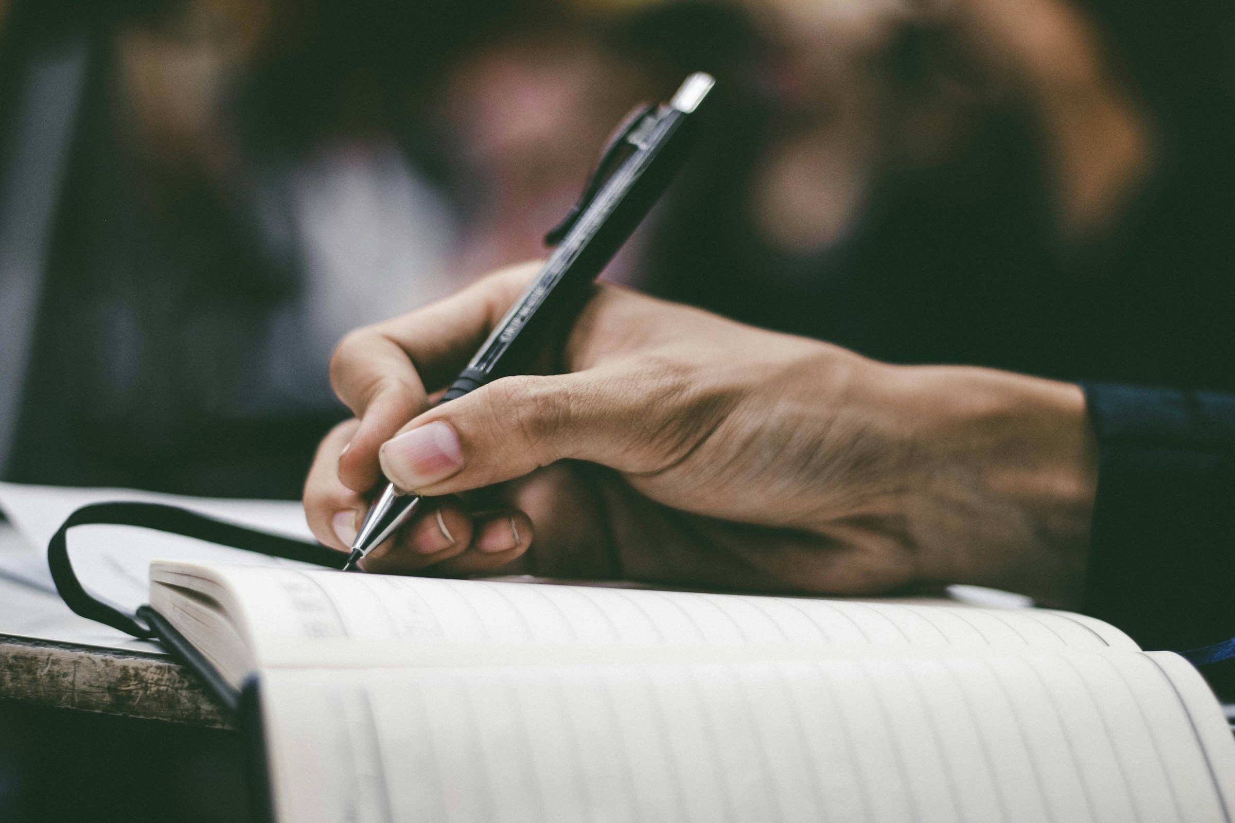 A hand writes in a lined notebook with a black pen.