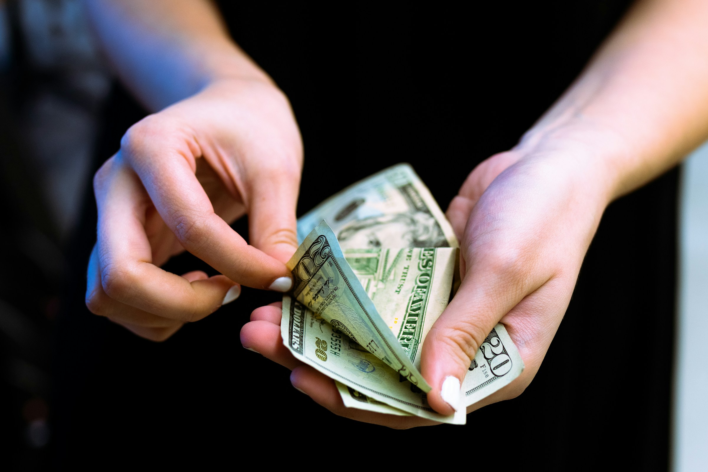 A person's hands flipping through a stack of $20 bills.