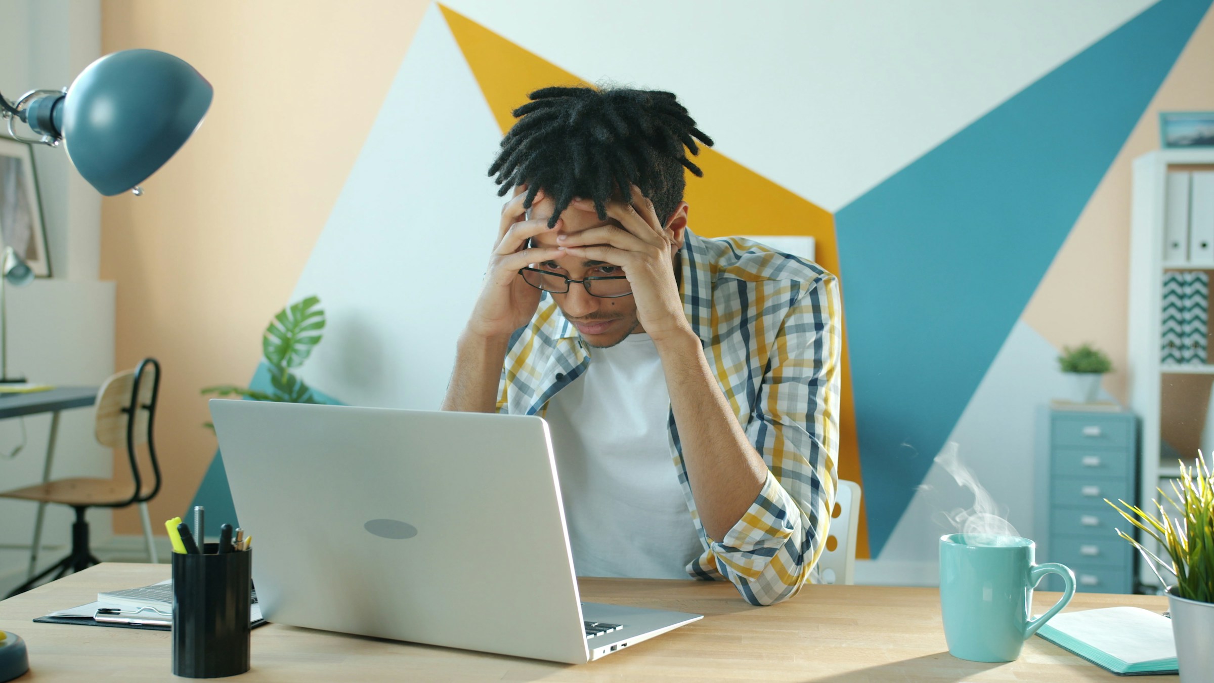 A distressed-looking person holds their head while looking at a laptop screen.