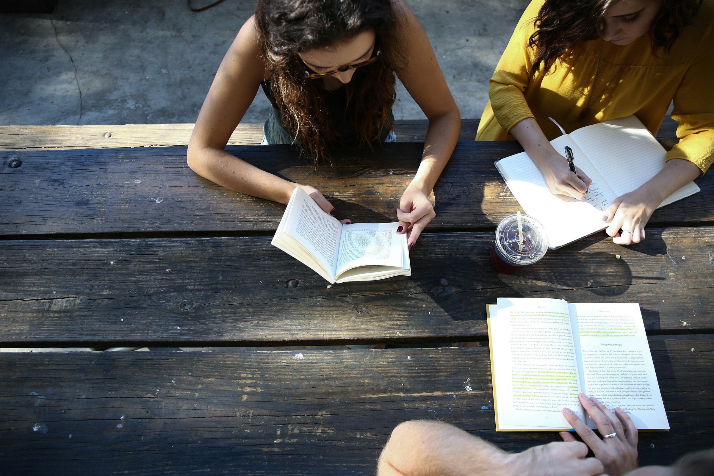 Three people sit around a picnic table writing in notebooks.